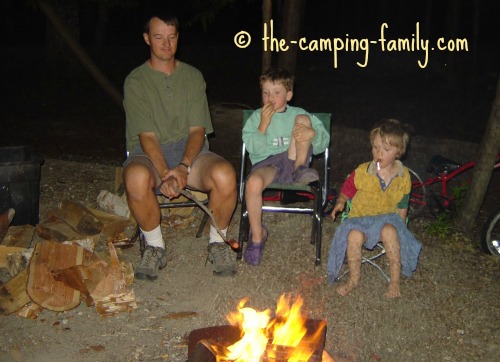 family roasting hot dogs over the fire