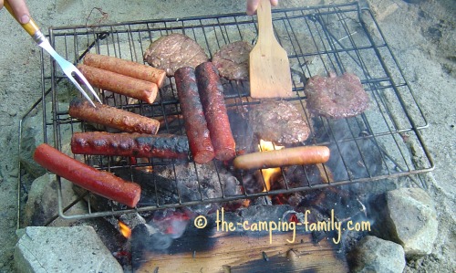 burgers and hotdogs on a grill over a campfire