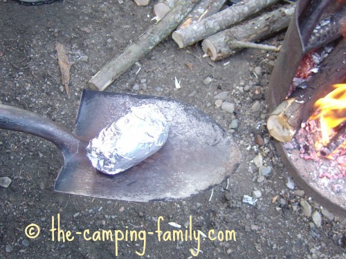 removing foil-wrapped potato from campfire with spade