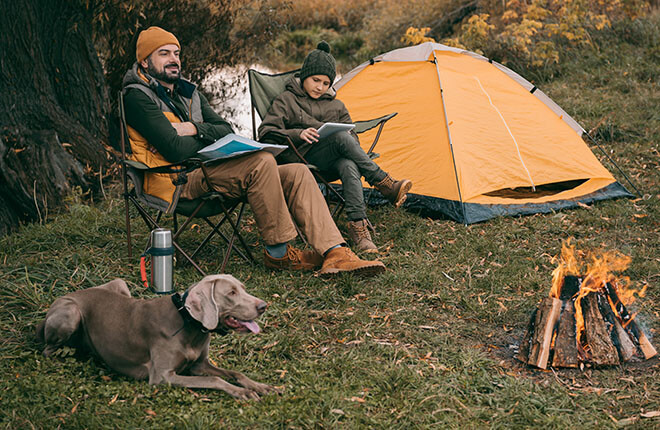 A man sitting in a camping chair with a tent in the background and a dog