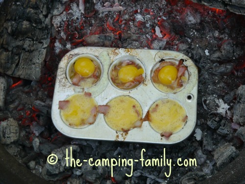 muffin tin bacon and eggs cooking on campfire