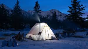 winter camping in the evening with a dark blue sky above a white tent