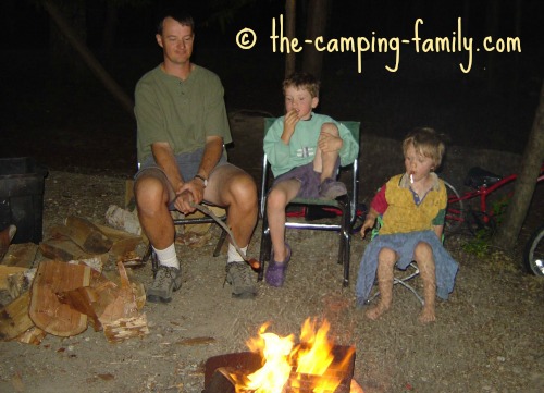 family roasting hot dogs around the campfire
