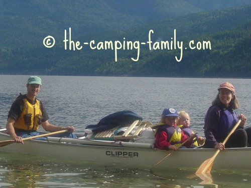 family in canoe with folding chairs lashed to pile of gear